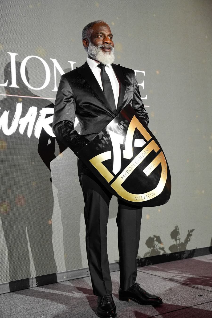 Myron Golden in a black suit holding his golden shield award